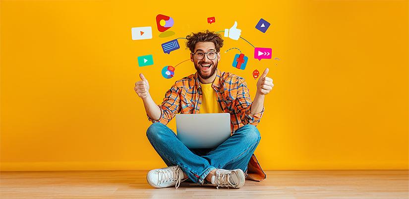 Smiling man sitting on the ground with his laptop having fun with social media apps